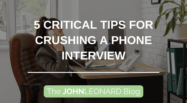 Person in a professional office setting taking a phone call at a desk, with overlaid text reading “5 Critical Tips for Crushing a Phone Interview” and “The JOHNLEONARD Blog.”