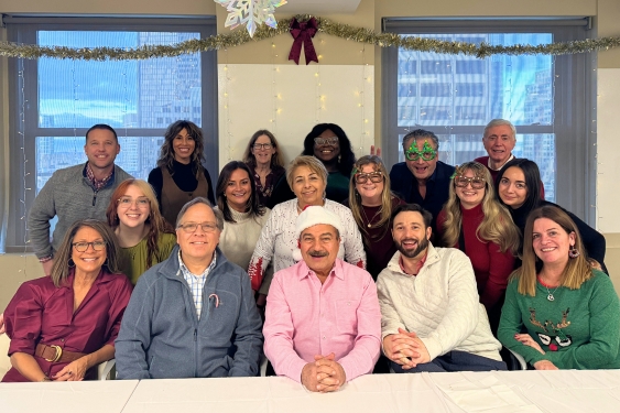 2025 JOHNLEONARD Holiday Party Group photo of JOHNLEONARD team members gathered indoors at a holiday celebration, with festive decorations including garland, lights, and a snowflake.