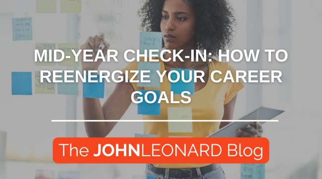 Professional woman reviewing sticky notes on glass wall with tablet in hand. Text overlay reads: Mid-Year Check-In: How to Reenergize Your Career Goals – The JOHNLEONARD Blog.