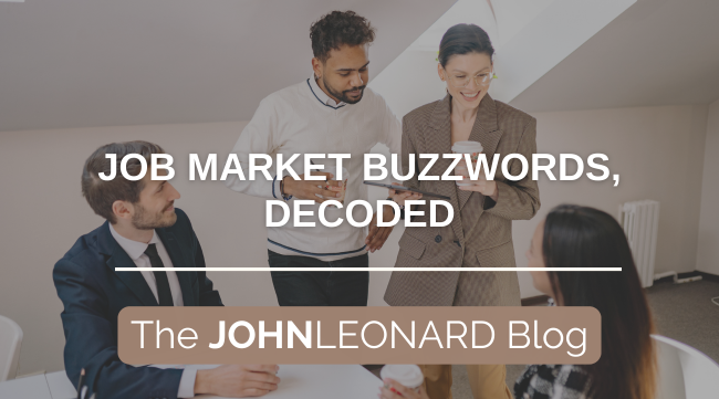 Four professionals gathered around a table in a modern office, collaborating and smiling. Overlaid text reads “JOB MARKET BUZZWORDS, DECODED” and “The JOHNLEONARD Blog.”