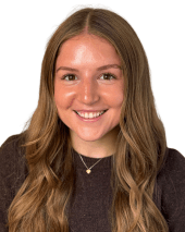Professional headshot of Carly Brady, a person smiling, with long hair and a brown sweater, on a white background.